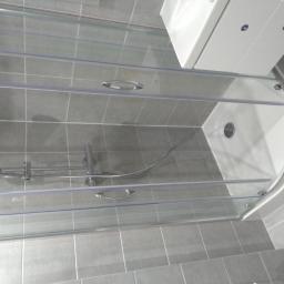 Piotr i Paweł - Szara łazienka z kabiną prysznicową z przesuwnymi drzwiami, widoczna bateria natryskowa i biała umywalka z szafką.