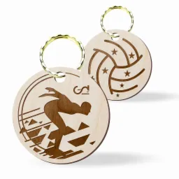 Dwa drewniane breloczki z wygrawerowanymi motywami: siatkarz w akcji i piłka do siatkówki z gwiazdkami, zawieszone na złotych kółkach.