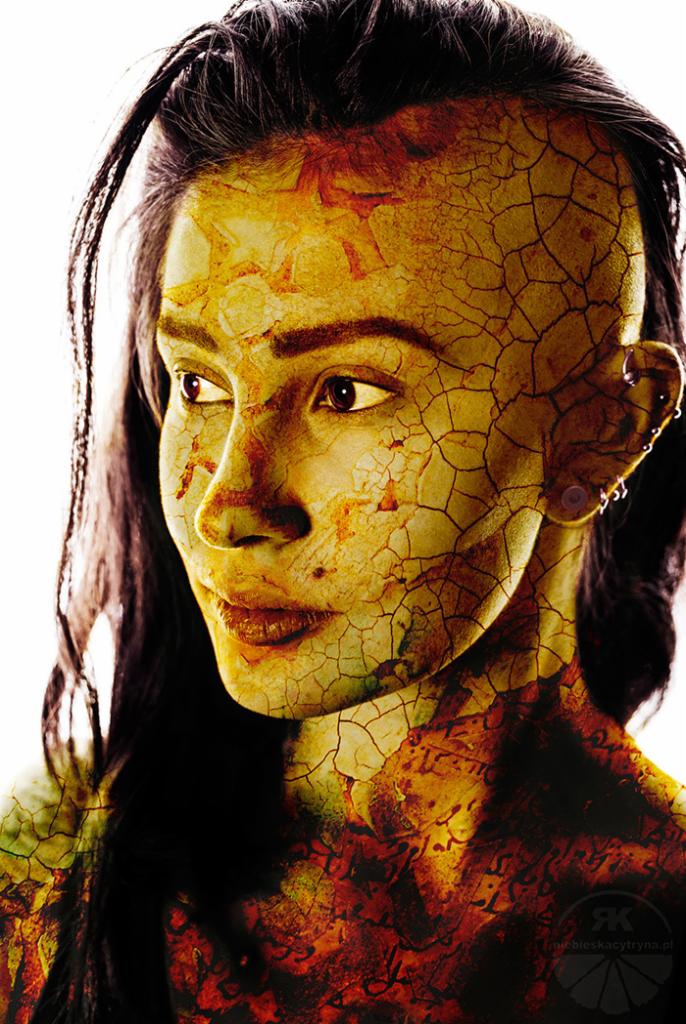 Portret kobiety z artystycznym efektem pęknięć na skórze, nałożonym w postprodukcji, z widocznymi kolczykami w uchu i ciemnymi włosami na jasnym tle.
