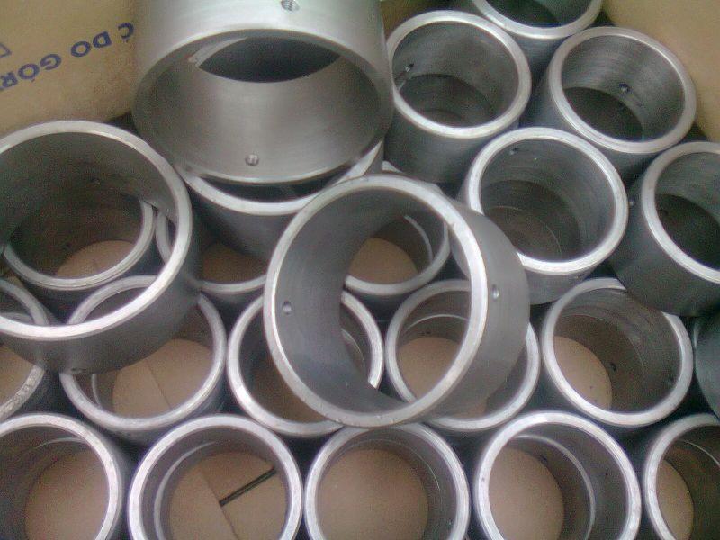 Partia metalowych tulei z otworem, ułożonych w kartonowym pudle, widoczne ślady obróbki.