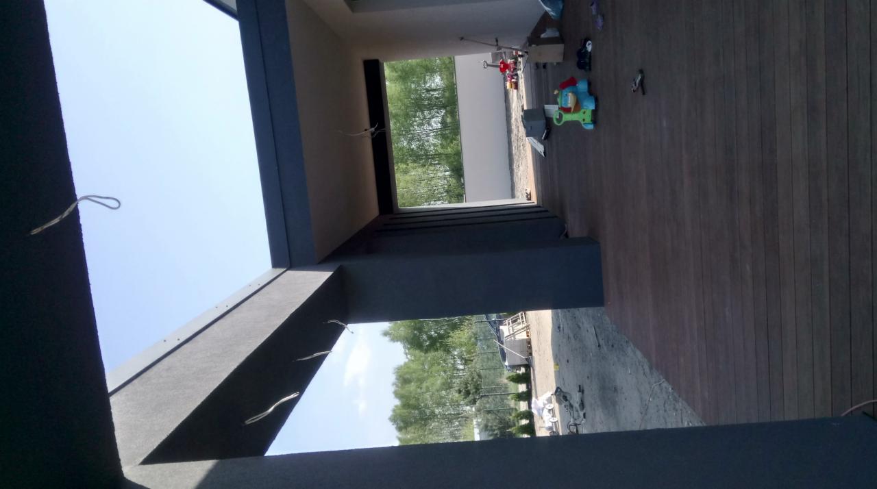 Szare elementy konstrukcyjne domu w surowym stanie, widok na zewnątrz przez otwory okienne, częściowo widoczny drewniany taras z zabawkami.