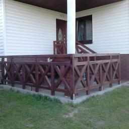USŁUGI STOLARSKIE Stanisław Sikora - Drewniana balustrada z krzyżowym wzorem na niskim tarasie przy domu z sidingiem, widoczny fragment schodów i filar podtrzymujący zadaszenie.
