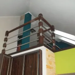 Wewnętrzna balustrada z drewnianymi słupkami i metalowymi poprzeczkami, zamontowana nad szafą wnękową, z widocznym fragmentem ściany w kolorze limonki i dekoracyjną ścianą w tle.