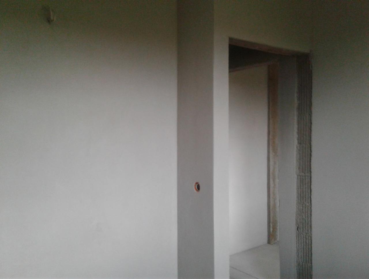 Świeżo otynkowana ściana w szarym odcieniu z widocznym otworem na gniazdko elektryczne i surową ościeżnicą drzwiową w tle.