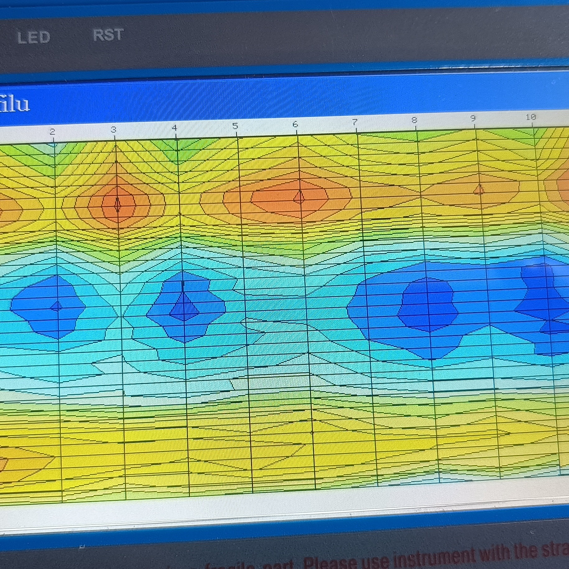Ekran urządzenia pomiarowego z kolorową mapą konturową, prawdopodobnie przedstawiającą wyniki pomiarów geofizycznych lub geologicznych, z dominującymi kolorami żółtym, pomarańczowym i niebieskim.