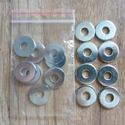 Ewa Szwon Firma Handlowa - Metalowe podkładki w przezroczystym, zamykanym woreczku foliowym oraz ułożone obok na drewnianej powierzchni.