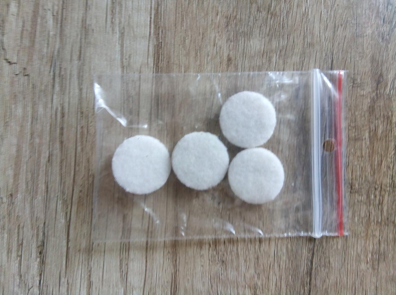 Cztery białe, okrągłe filcowe podkładki w przezroczystym woreczku strunowym na drewnianym tle.