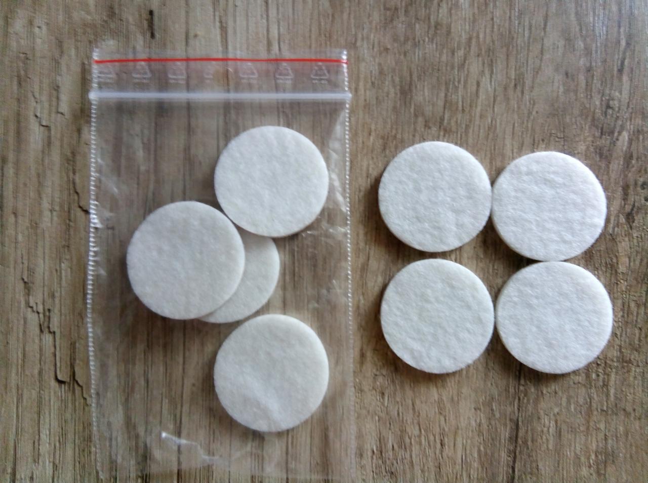 Białe, okrągłe wkładki filcowe, część w przezroczystym woreczku strunowym, ułożone na drewnianej powierzchni