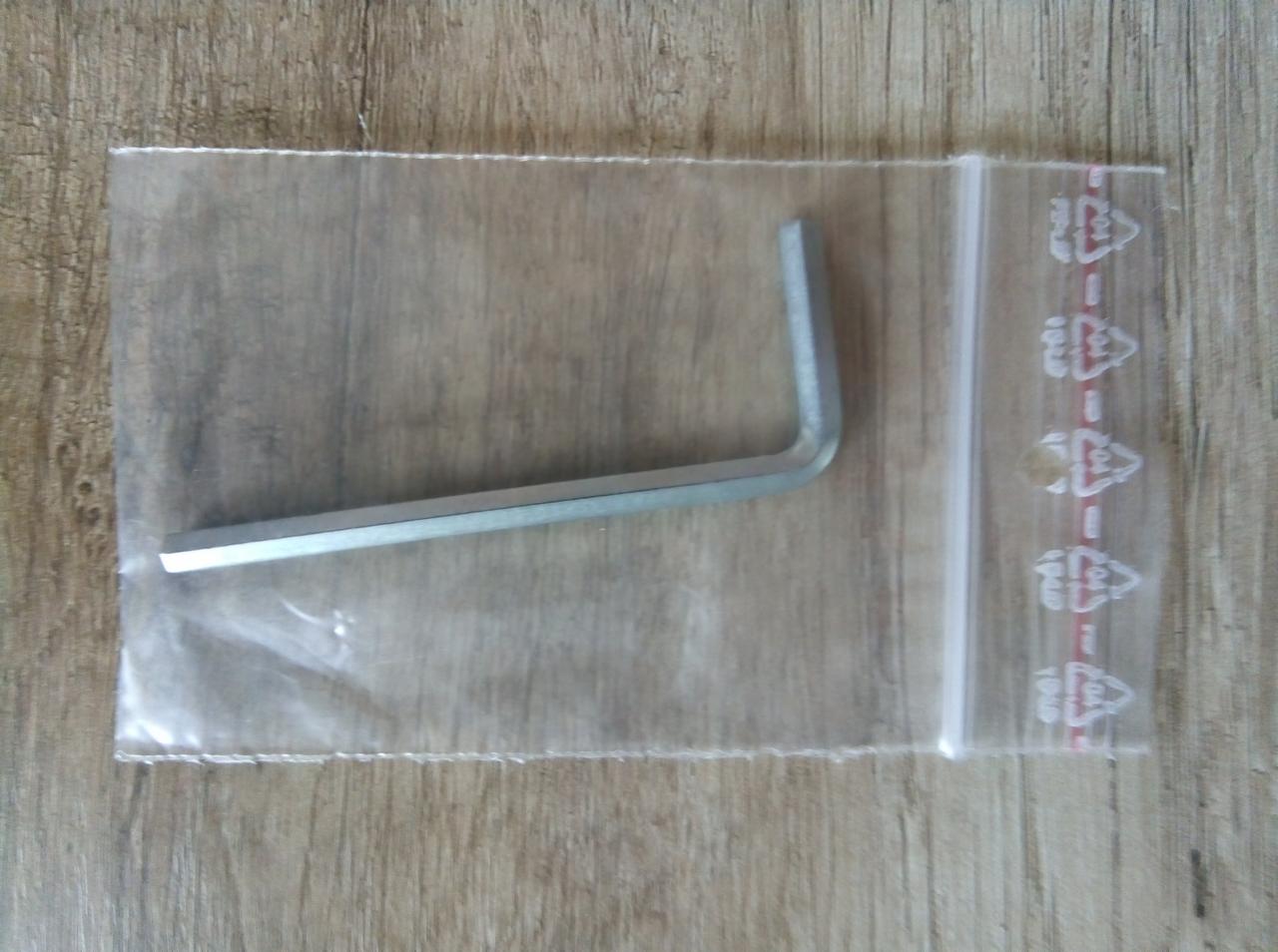 Klucz imbusowy zapakowany w przezroczysty woreczek strunowy z oznaczeniami recyklingu, leżący na drewnianym podłożu.