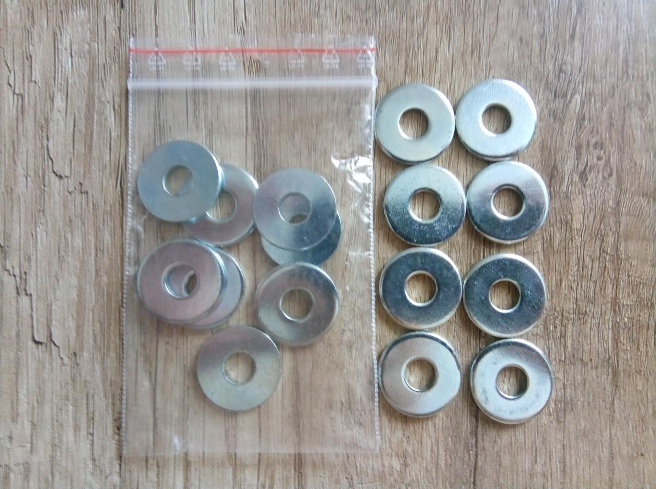 Metalowe podkładki w przezroczystym, zamykanym woreczku foliowym oraz ułożone obok na drewnianej powierzchni.