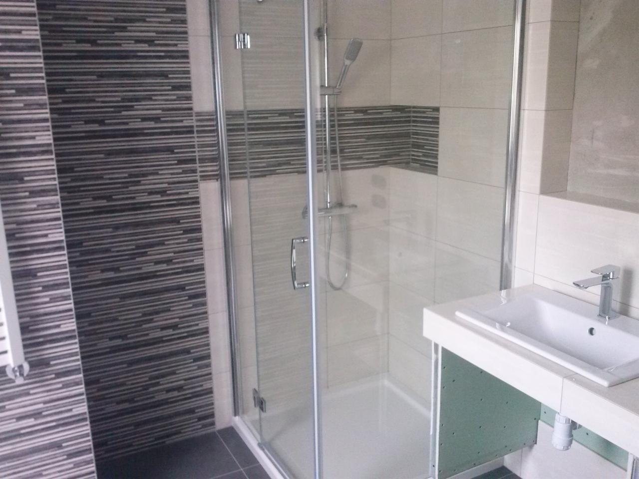 Nowoczesna łazienka z kabiną prysznicową ze szklanymi drzwiami, umywalką na blacie i płytkami imitującymi drewno na ścianie.