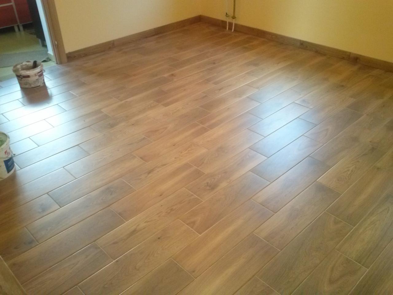 Ułożona podłoga z płytek imitujących drewno w nowym pomieszczeniu, widoczne wiaderka z farbą i zaprawą w rogu.
