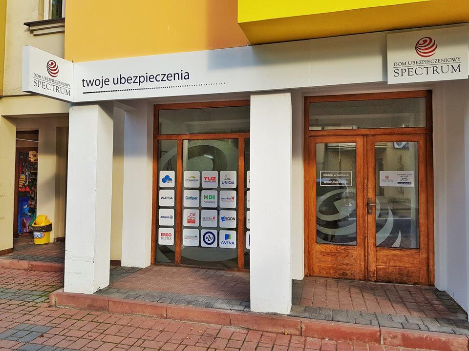 Fasada biura ubezpieczeniowego Spectrum z widocznymi logotypami różnych towarzystw ubezpieczeniowych na szybie i szyldzie informacyjnym.