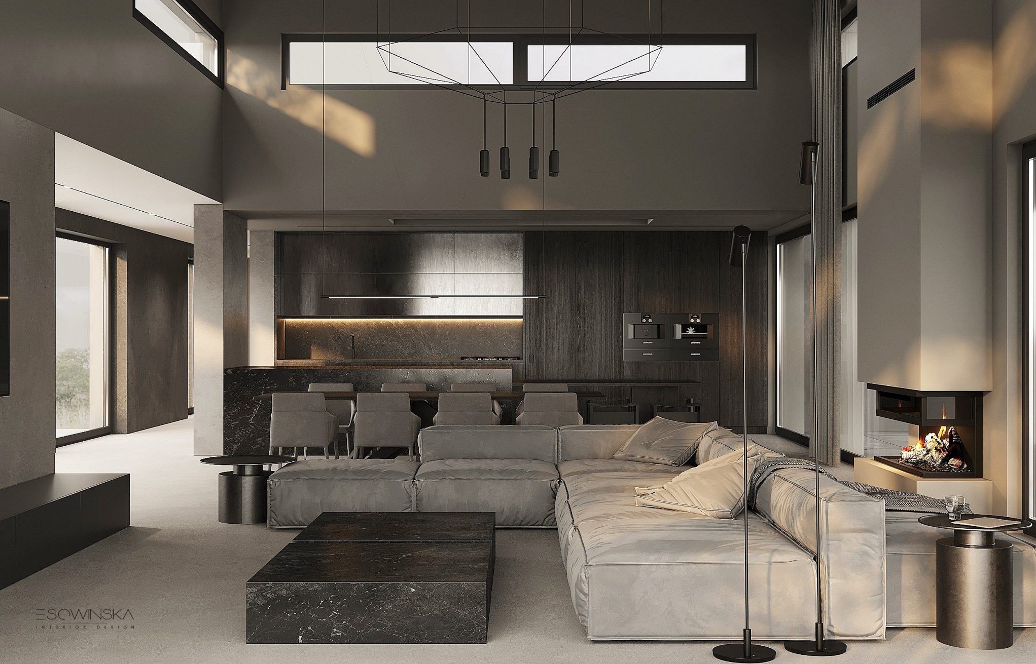 Przestronny salon z otwartą kuchnią w odcieniach szarości, z dużym narożnikiem, marmurowym stolikiem kawowym i kominkiem, oświetlony nowoczesną lampą wiszącą i wysokimi oknami.