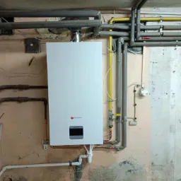 Nowy, biały piec gazowy zamontowany na ścianie z widocznymi rurami, w surowym pomieszczeniu z instalacją gazową.