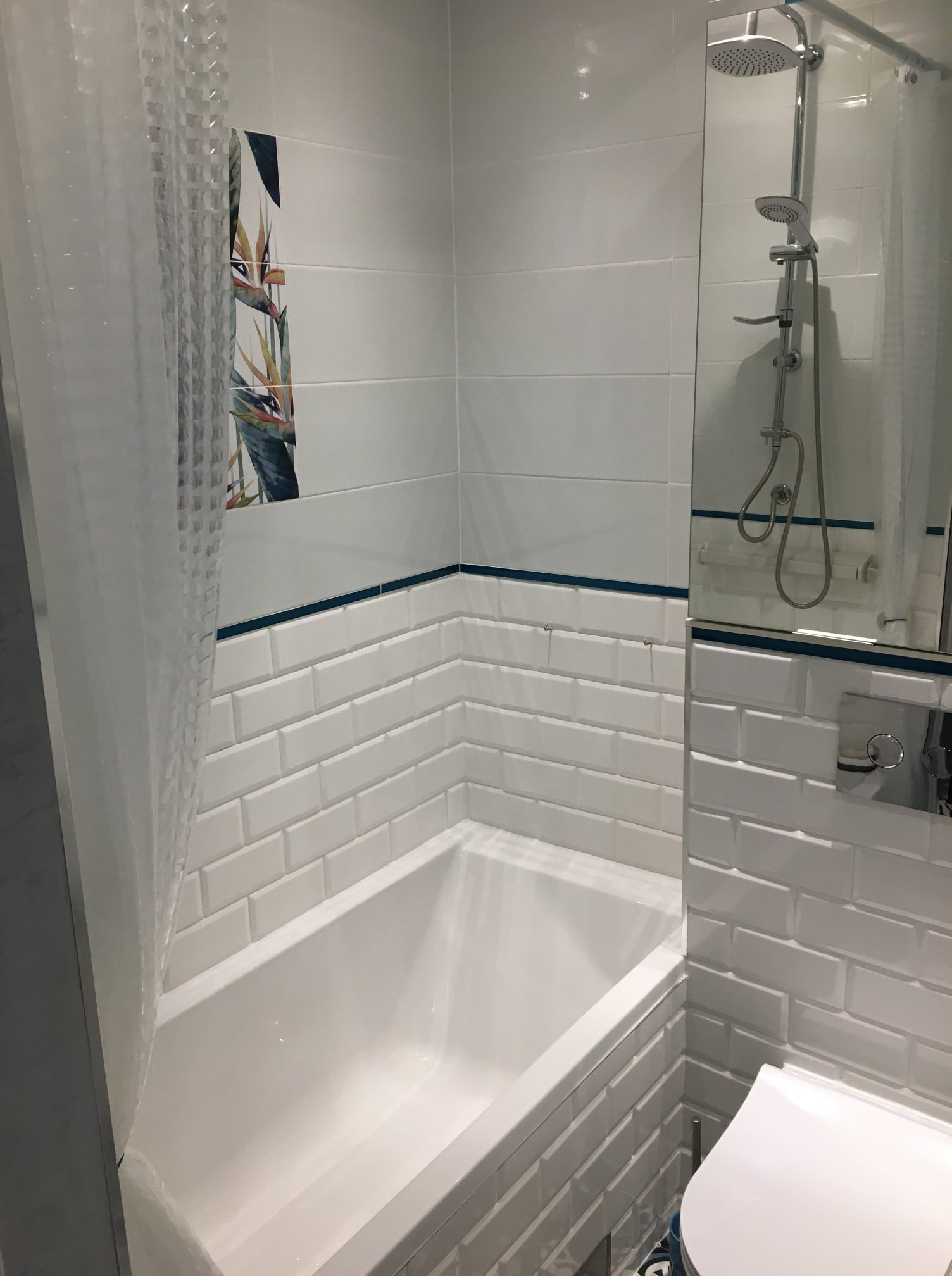 Nowoczesna łazienka z białą armaturą, płytkami typu metro z granatowym akcentem i zasłoną prysznicową z wzorem roślinnym.