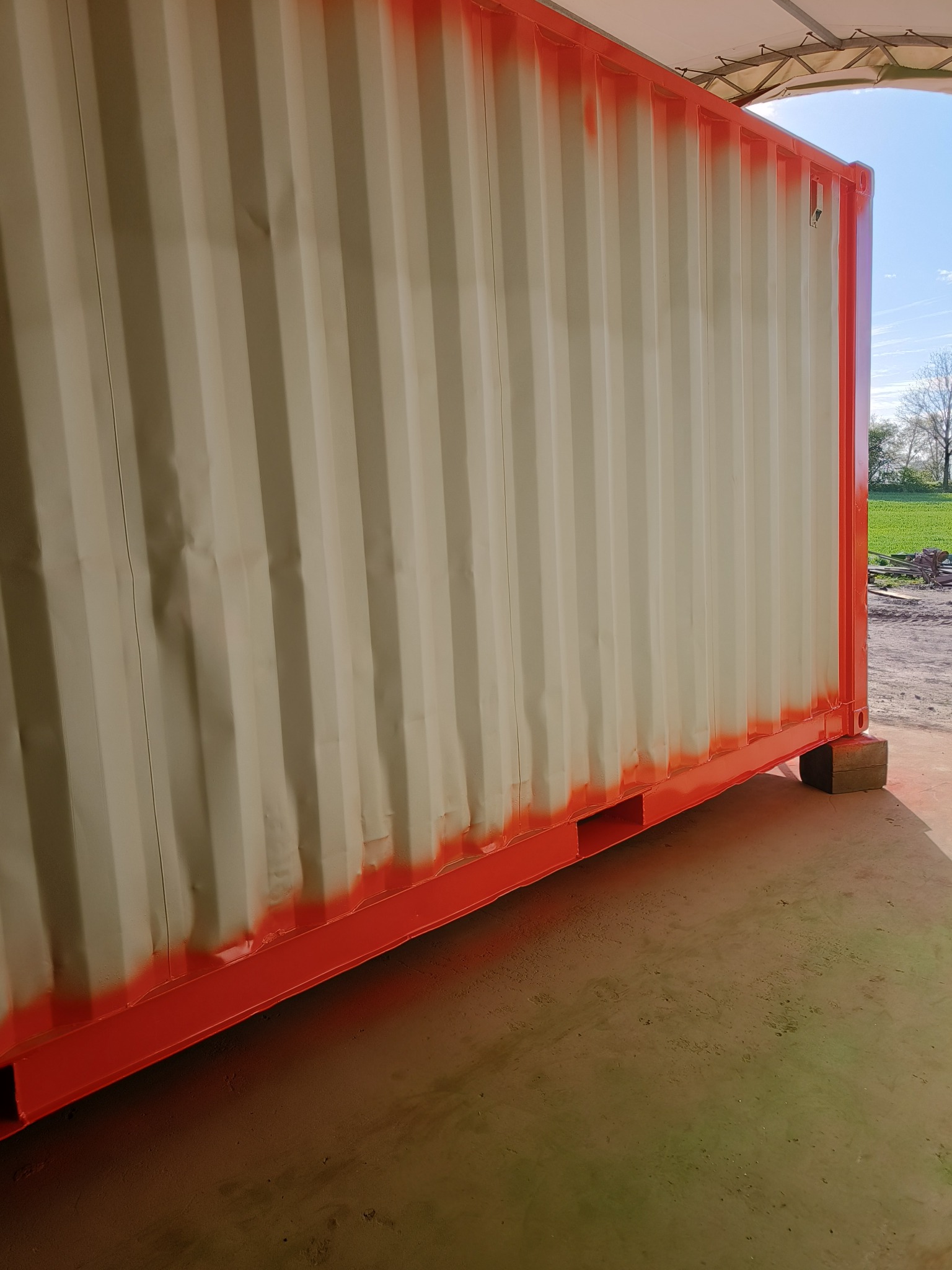 Odświeżony kontener magazynowy z pomalowanymi na czerwono krawędziami i ramą, stojący na betonowych blokach na zewnątrz budynku.