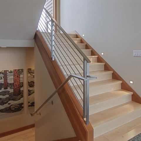 Nowoczesne schody z drewnianymi stopniami i balustradą z poziomych, metalowych prętów; w tle widoczny obraz z motywem drzew.