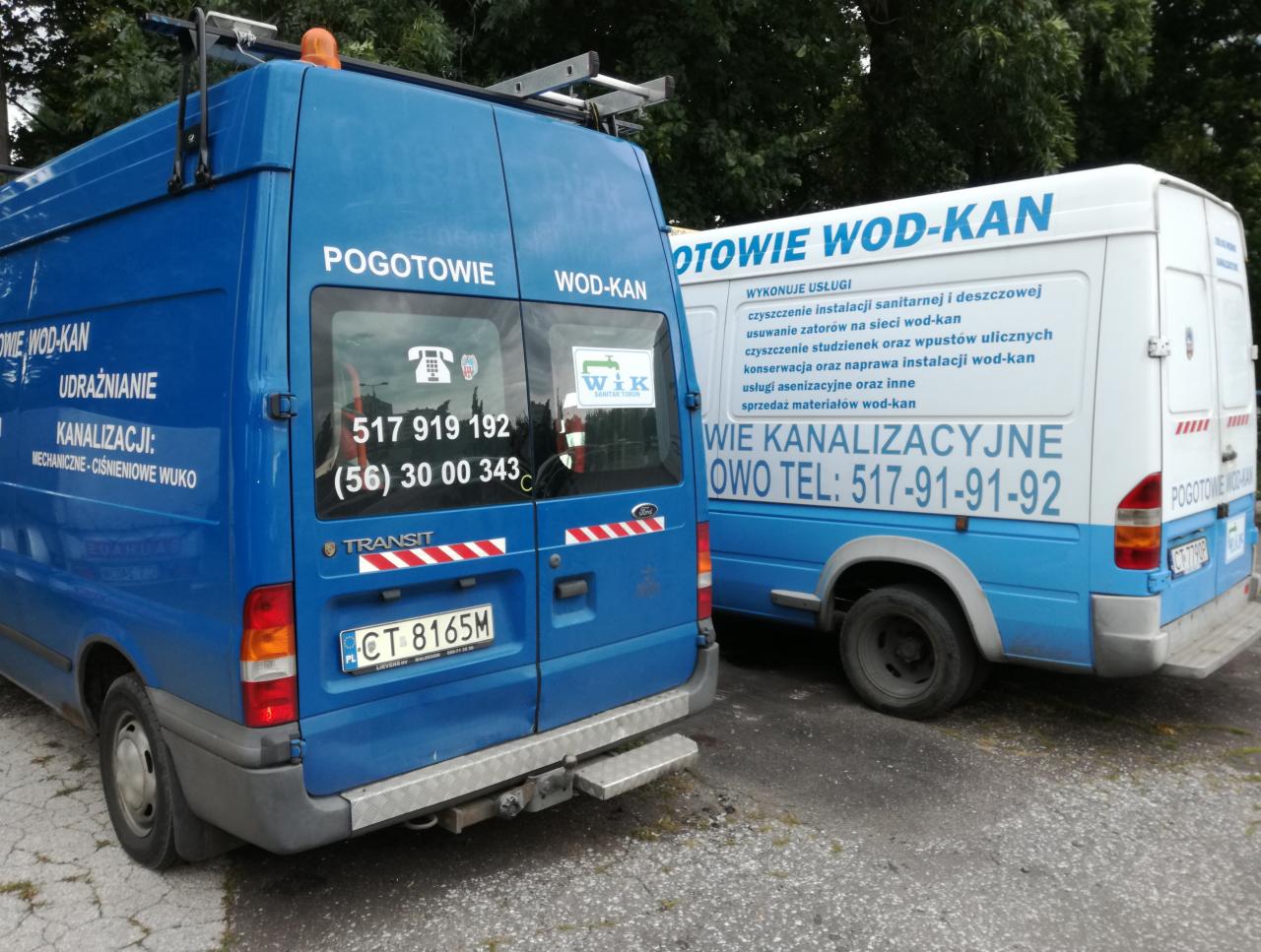 Dwa busy pogotowia wodno-kanalizacyjnego zaparkowane obok siebie, z widocznymi numerami telefonów i informacjami o świadczonych usługach udrażniania kanalizacji i czyszczenia instalacji.