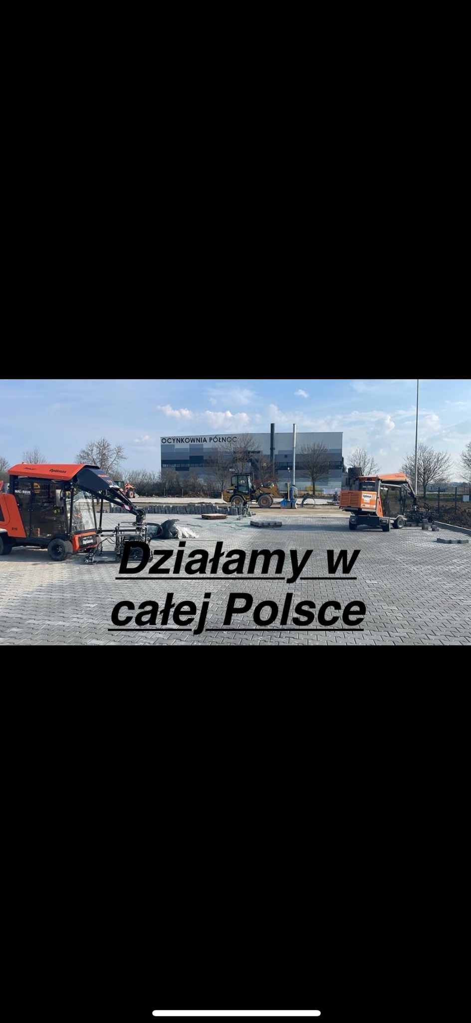 Maszyny brukarskie i koparka na placu budowy z częściowo ułożoną szarą kostką brukową, w tle budynek OCYNKOWNIA PÓŁNOC.