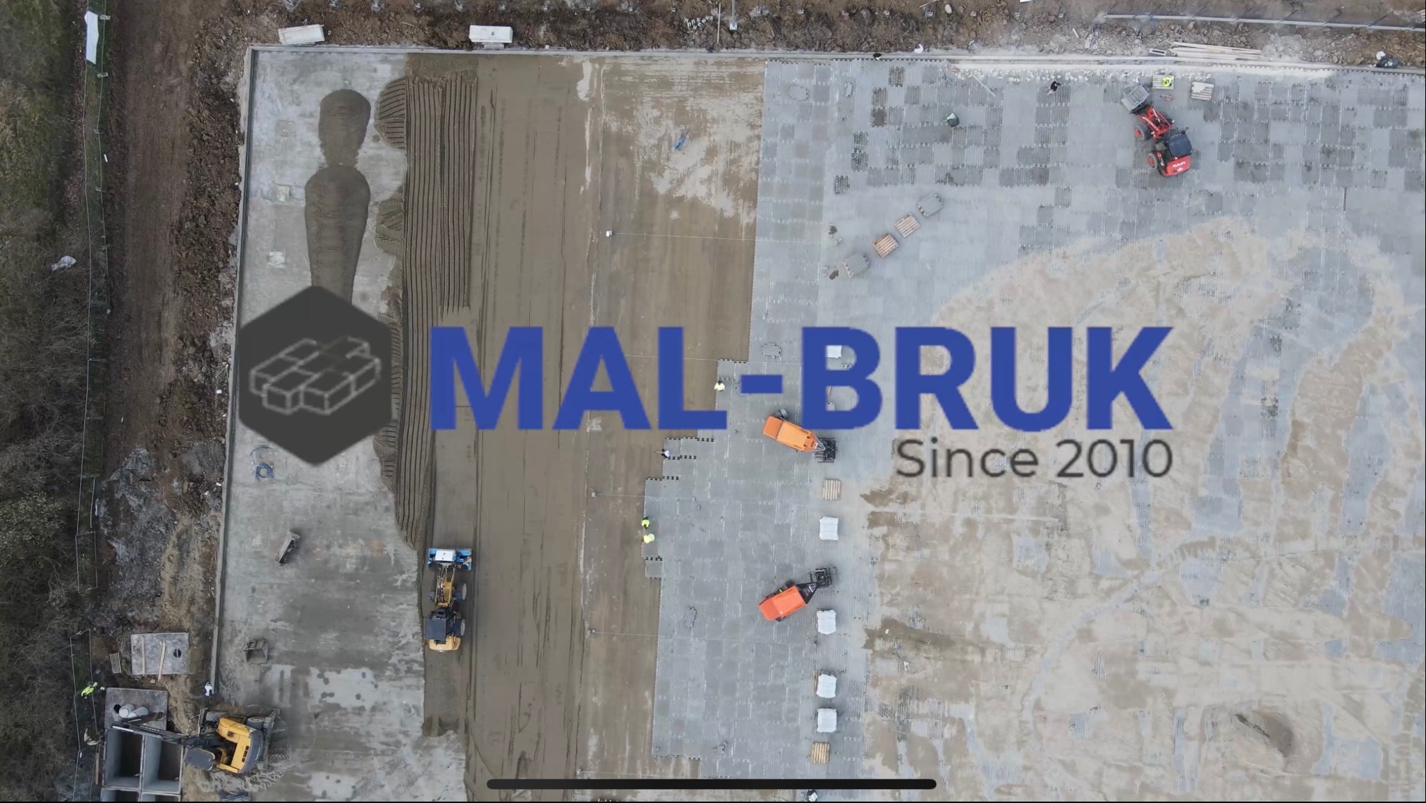 Widok z góry na plac budowy z częściowo ułożoną kostką betonową, rozplantowanym piaskiem i pracującymi maszynami budowlanymi, w tle widoczny las. Na zdjęciu nałożone logo firmy MAL-BRUK.