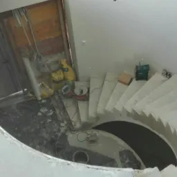 Wewnętrzne schody spiralne w trakcie wylewania betonu, widok z góry, widoczne narzędzia i materiały budowlane, ściany w stanie surowym.