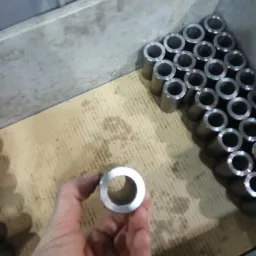 Ręka trzyma metalowy pierścień na tle pojemnika z dużą ilością podobnych elementów.