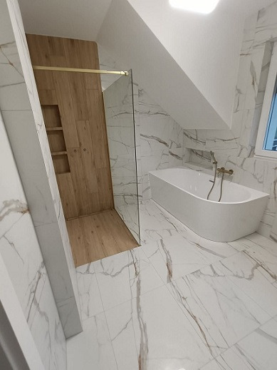 Nowoczesna łazienka z kabiną prysznicową typu walk-in z drewnianym wykończeniem i półkami wnękowymi, biała wolnostojąca wanna z mosiężną armaturą, oraz białe płytki imitujące marmur na ścianach...
