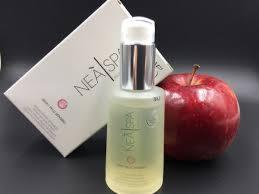 Butelka z płynem NEA SPA z srebrną pompką na tle pudełka tej samej marki i czerwonego jabłka na czarnym tle.