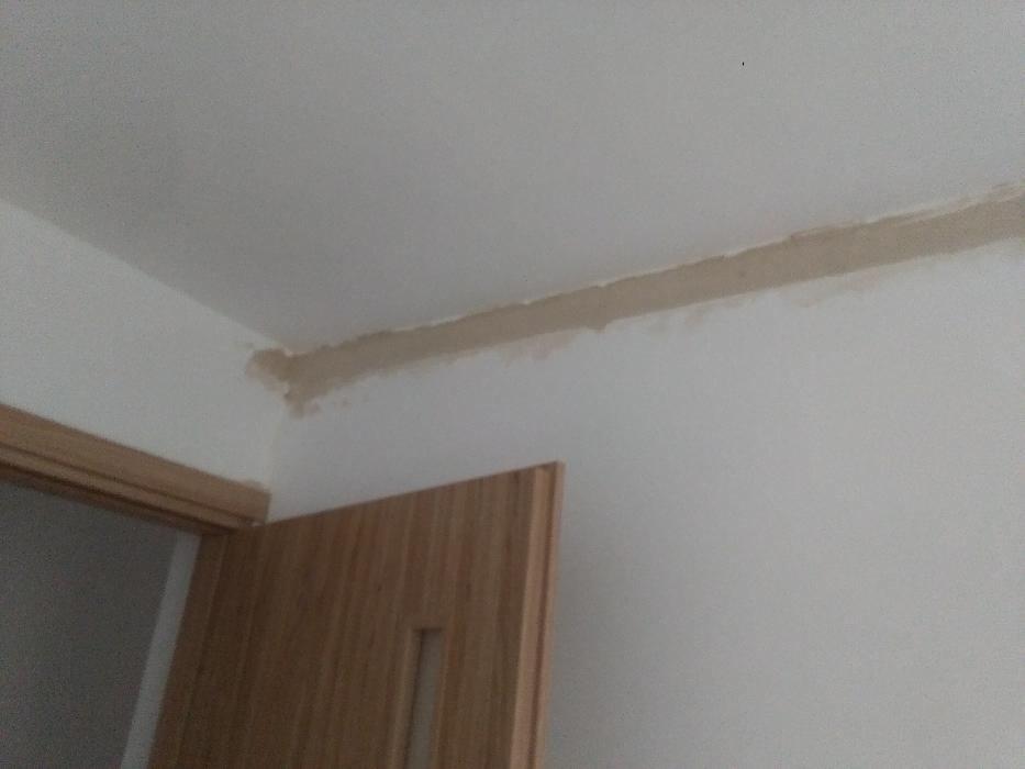 Wnętrze pokoju w trakcie wykańczania: szpachlowana listwa sufitowa, ściana pomalowana na biało, widoczna drewniana ościeżnica drzwi.