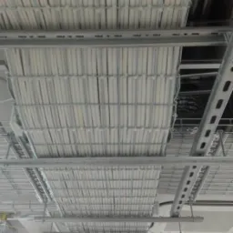 Równolegle ułożone, białe rury w metalowej siatce pod sufitem w przestrzeni biurowej, widok z dołu.