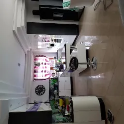 Nowoczesna kuchnia z białymi meblami, czarnymi akcentami i zegarem na ścianie, widok z góry na błyszczące płytki podłogowe.