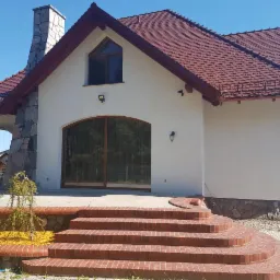 Elewacja domu jednorodzinnego w Sławie po renowacji, z widocznymi schodami z cegły klinkierowej i kamiennym kominem.