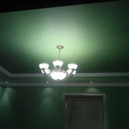 Zielony sufit z klasycznym żyrandolem i listwami dekoracyjnymi, oświetlony punktowymi lampami wzdłuż krawędzi.