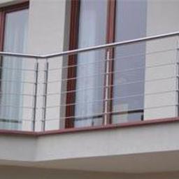 Zig zak elementy nierdzewne - Nowoczesny balkon z metalową balustradą z poziomych rurek, widok z zewnątrz, brązowe ramy okienne, elewacja w odcieniach beżu.