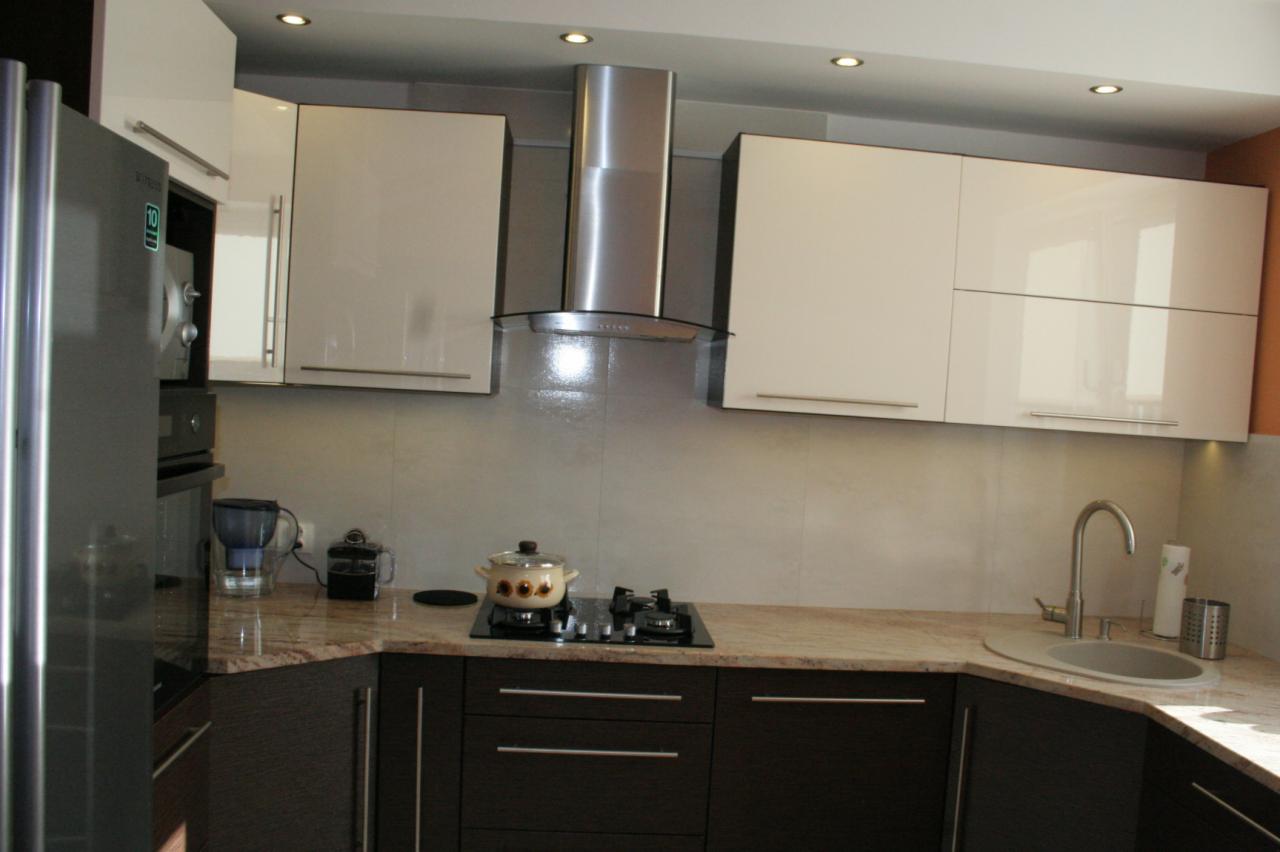 Nowoczesna kuchnia z białymi szafkami wiszącymi i ciemnobrązowymi szafkami dolnymi, marmurowy blat, srebrny okap i kuchenka gazowa z garnkiem.