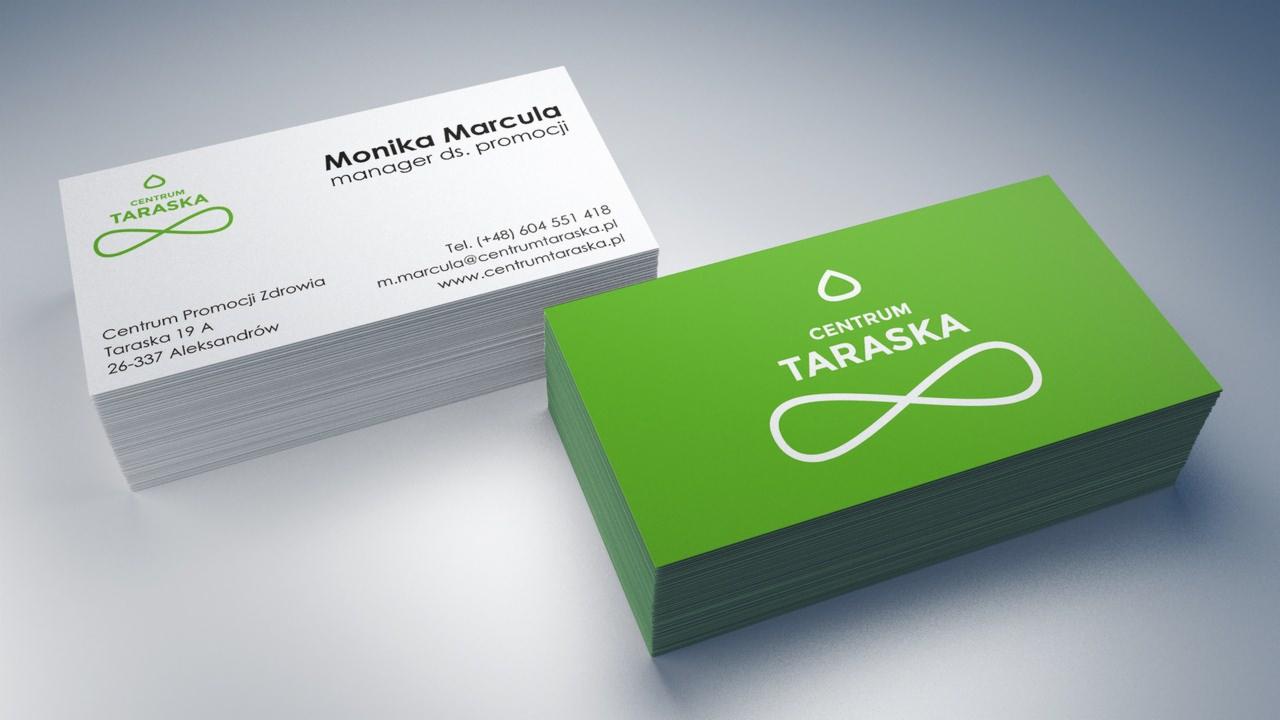 Dwa stosy wizytówek: białe z zielonym logo i danymi kontaktowymi oraz zielone z białym logo, ułożone na gładkim, szarym tle.
