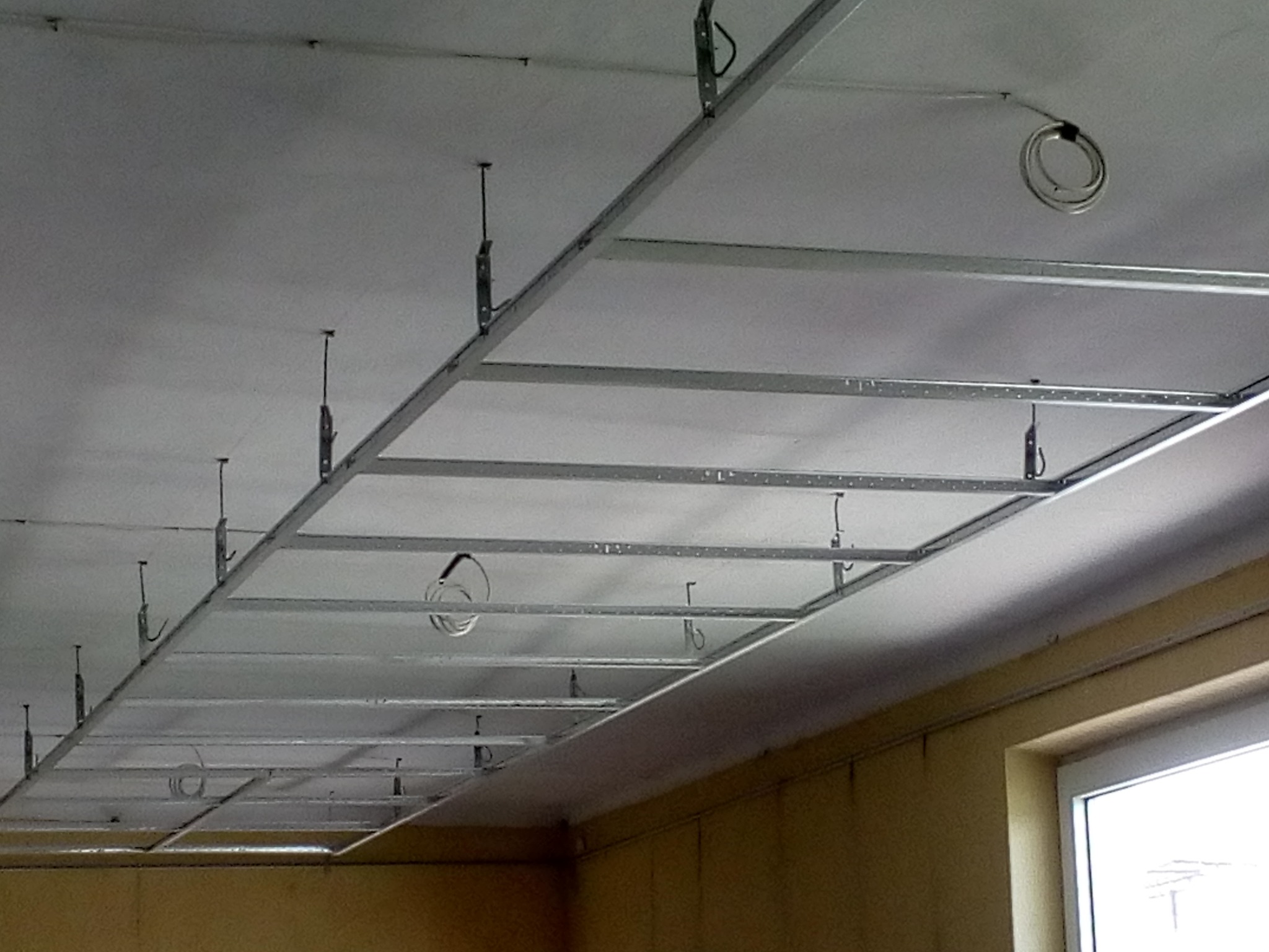 Metalowa konstrukcja sufitu podwieszanego z płyt kartonowo-gipsowych, widoczne przewody elektryczne, częściowo zamontowane płyty.