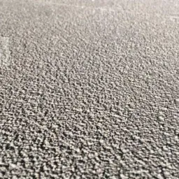 Szara, drobnoziarnista powierzchnia podłogi z perspektywy bliskiej, ukazująca nierównomierną teksturę i delikatne refleksy świetlne.