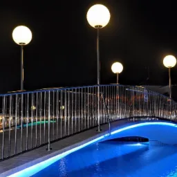 Oświetlony nocą mostek nad basenem z metalową balustradą i kulistymi lampami, podświetlony niebieskim światłem LED.