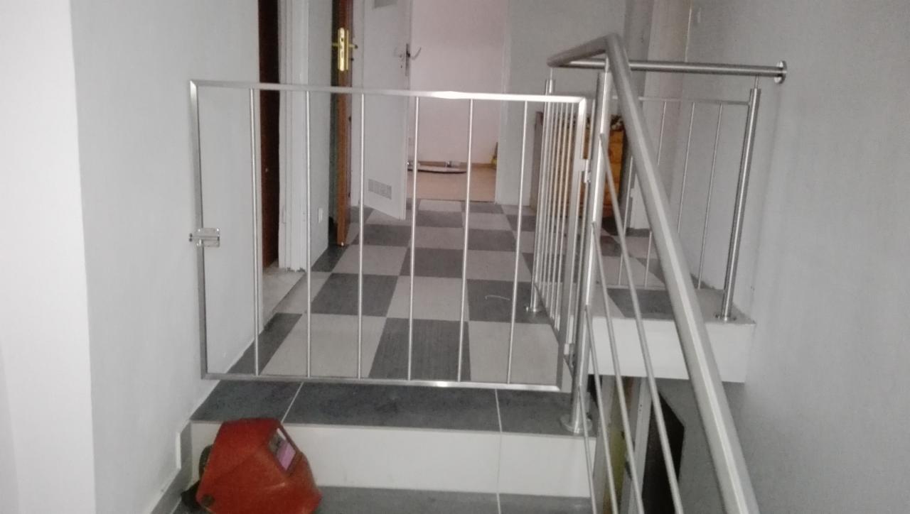 Metalowa barierka zabezpieczająca schody z widocznym kaskiem spawalniczym na stopniu, podłoga w szachownicę w tle.