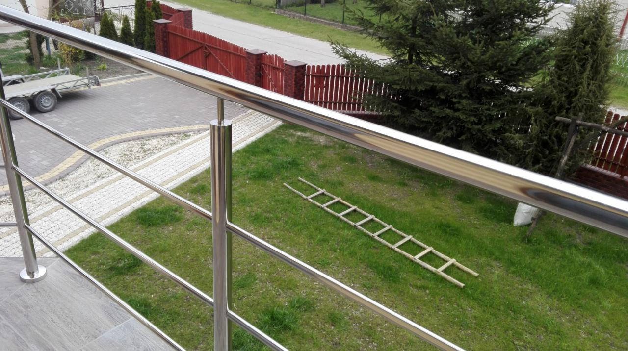 Błyszcząca, trójpoziomowa balustrada nierdzewna z widokiem na podjazd z przyczepą, czerwoną drewnianą bramę i rozłożoną drewnianą drabinę na trawniku.