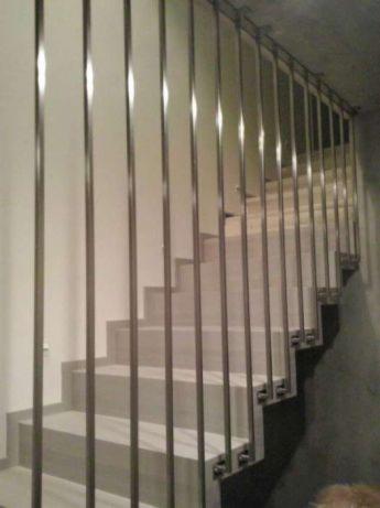 Nowoczesne schody z szarymi stopniami i minimalistyczną balustradą ze stali nierdzewnej z pionowymi prętami.