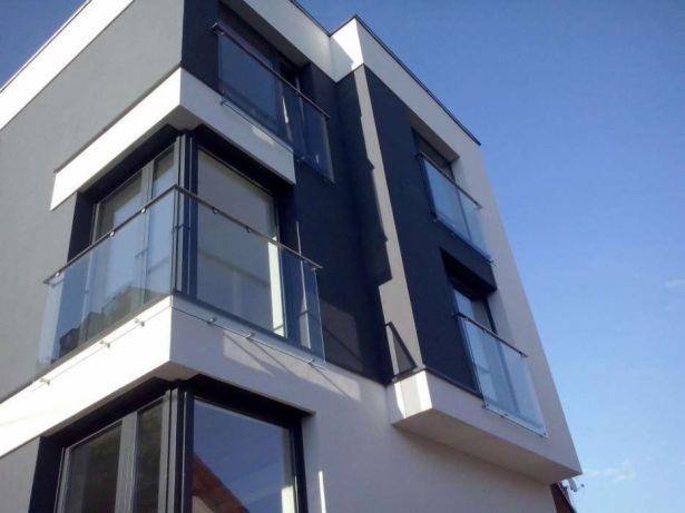 Nowoczesny budynek z balkonami zabezpieczonymi szklanymi taflami, widok z dołu na błękitne niebo.