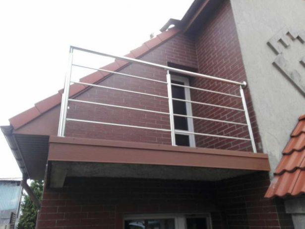 Balkon z balustradą nierdzewną, widok z dołu na ceglany budynek z brązowym podsufitką.