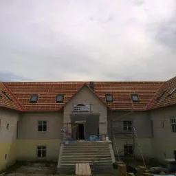 Budynek murowany w trakcie budowy, widoczne przygotowane podłoże pod dach z oknami dachowymi, ściany z bloczków betonowych, schody wejściowe i rusztowania.