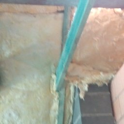 Wega Budownictwo - Izolacja poddasza wełną mineralną, widoczne drewniane elementy konstrukcyjne i fragment ściany z cegły. Ujęcie z dołu, podkreślające detale wykonania.