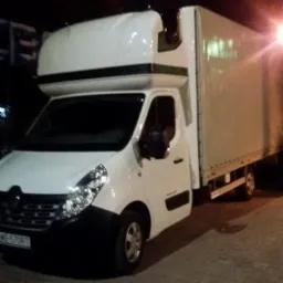 Biały samochód dostawczy Renault Master z zabudową kontenerową, sfotografowany nocą z niskiej perspektywy na brukowanym parkingu.