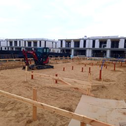 Hydro-Invest Łukasz Nowak - Fundamenty pod budowę szeregowców z widoczną instalacją hydrauliczną i mini koparką Yanmar na piaszczystym terenie. Ujęcie z poziomu gruntu, pochmurne niebo.