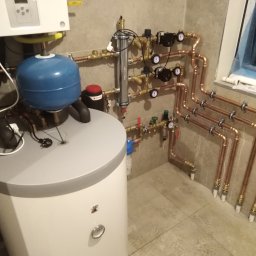 Hydro-Invest Łukasz Nowak - Nowoczesna kotłownia z piecem gazowym, zbiornikiem buforowym i miedzianą instalacją, widoczne manometry i zawory, świeżo po instalacji.
